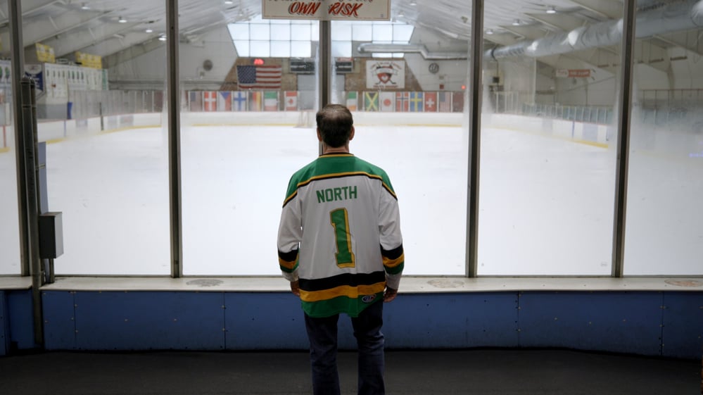 Alden Brown stands alone in a NORTH 1 hockey jersey looking out over an empty ice rink