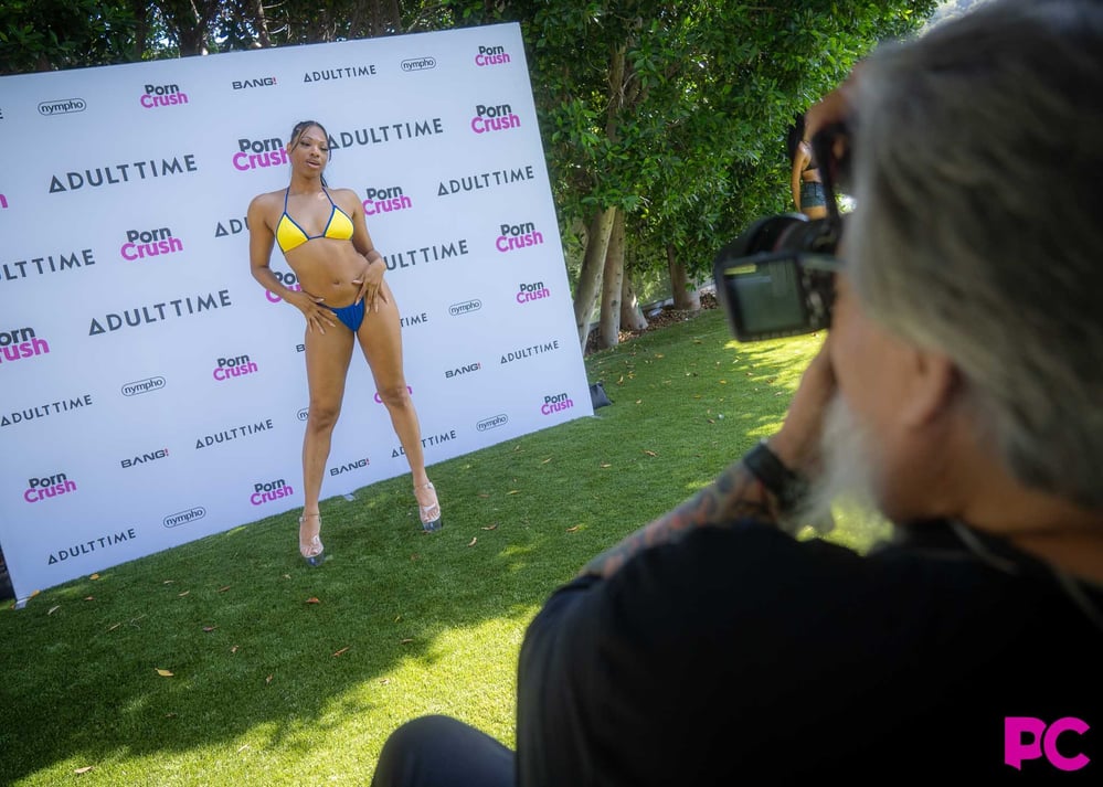 Photographer Rick Garcia shoots a performer against the PornCrush and Adult Time branded backdrop on the lawn at Media Day 2026.